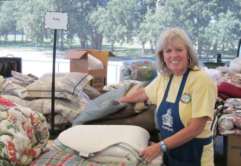 Patty Evans, Co-Chair for the Linens section, is shown stacking the king coverlet sets in the Linens section.