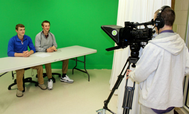 Samuel Nichols (left) and Zach Carson anchor video announcements for Athens High School as Edward Risner films. They are being filmed in front of a “green screen” so that graphics can be added digitally. (Julie Whitley/AISD)